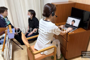 介護施設の個室で、利用者と介護職員がお話している様子と、手前にかけつけた看護師がノートパソコンを開いてインカムをつけ、画面ごしに医師と会話している様子を写した写真。かけつけの様子をあらわしています